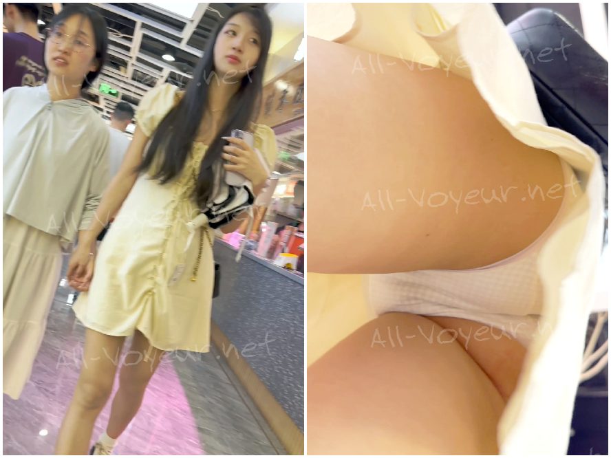 サンドドレスを着た若い女性が一人で買い物をしながらスナックを食べています。彼女のピンクの薄い裏地は少し透けていて、低い角度で CD をかけています。